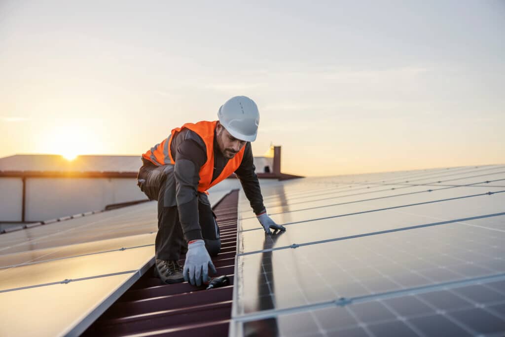 The worker is installing solar panels on the rooftop.