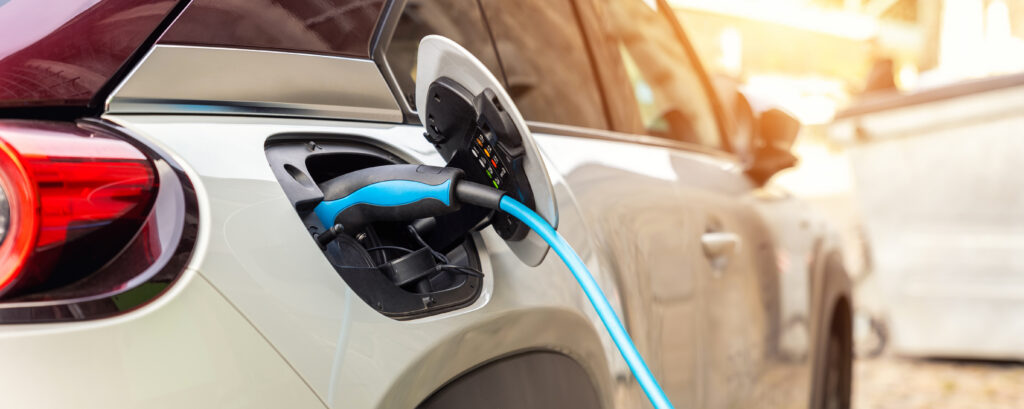 Close-up modern electric plug-in hybrid car parked near fast charger charging station point in center street old European city. Eco friendly green energy vehicle. Zero emission transport technology.