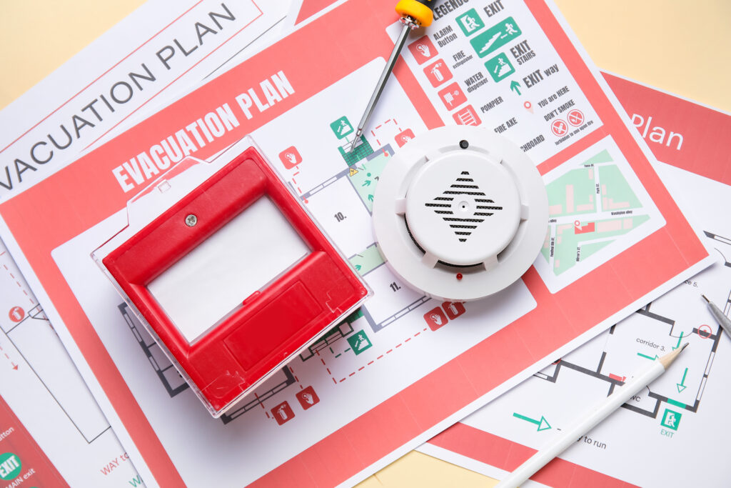 What is a PEEP and Who Needs One? Modern smoke detector with fire call point and evacuation plans on yellow background